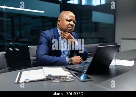 Un uomo d'affari maturo di colore che tocca il mento mentre esamina le informazioni sul notebook Foto Stock