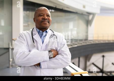Medico nero in piedi con sicurezza con le braccia incrociate, con camice da laboratorio e stetoscopio Foto Stock