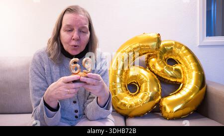 Donna anziana che fa saltare le candele su un cupcake per il suo 69esimo compleanno Foto Stock