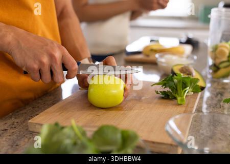 Coppia che prepara il pasto nella cucina casalinga, uomo in camicia arancione che affetta mela verde con un coltello dello chef Foto Stock