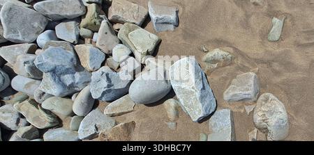 Pietre da spiaggia lisce di varie dimensioni e forme si trovano sparse sulla sabbia, creando una scena naturale e strutturata Foto Stock