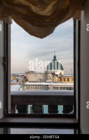 Vista da una finestra incorniciata da tende che mostrano i tetti e la cupola verde di un edificio storico a San Pietroburgo. La Chiesa di Santa Caterina, una A. Foto Stock