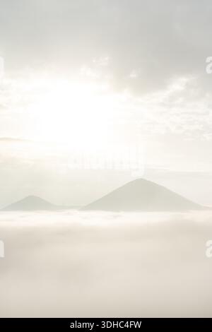 Paesaggio da sogno con due montagne in piedi sopra la nebbia con il sole che splende attraverso le nuvole sopra Foto Stock