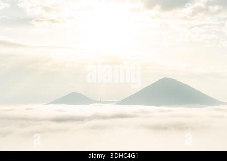 Paesaggio da sogno con due montagne in piedi sopra la nebbia con il sole che splende attraverso le nuvole sopra Foto Stock
