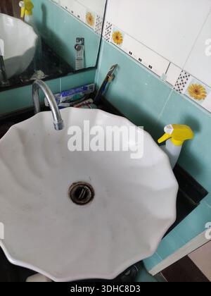 Lavandino bianco a forma di fiore in bagno con piastrelle color acqua e spray per la pulizia Foto Stock