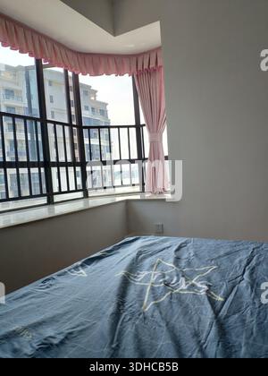 Accogliente camera da letto con finestra a bovindo e tende rosa che si affacciano sugli edifici urbani Foto Stock