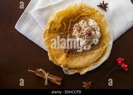 Pancake sottili con cannella panna montata e scaglie di cioccolato su un tavolo di legno scuro Foto Stock