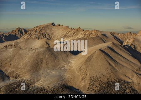 La vista aerea delle cime illuminate dal sole e delle valli ghiacciate scolpisce un maestoso paesaggio sotto un cielo tranquillo, Sierra Nevada, California, Stati Uniti. Foto Stock