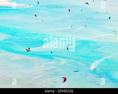 Vista aerea dei kiteboarders che ballano attraverso le acque turchesi, i loro aquiloni colorati punteggiano l'ampio oceano come vivaci pennellate, Parco natur Foto Stock