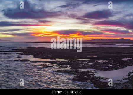 Vista aerea del faro di Faro de Toston, alto tra la costa frastagliata, baciato dalle vivaci sfumature del tramonto, che illuminano il ro scuro Foto Stock
