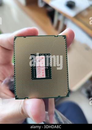 Primo piano di un processore CPU tenuto in mano, con spille e etichette dorate Foto Stock