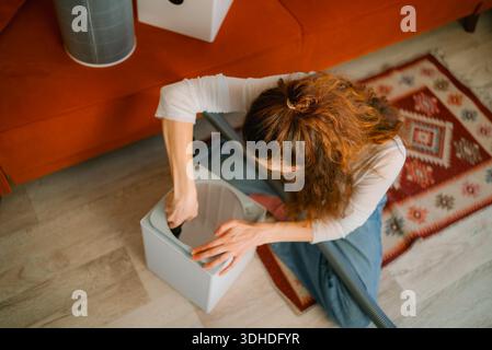 Donna che esegue la manutenzione essenziale aspirando polvere e particelle da un filtro del purificatore d'aria, contribuendo a migliorare la qualità dell'aria interna e creando un ambiente domestico sano Foto Stock