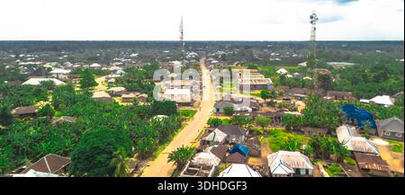 Vista aerea di una strada che biseca la lussureggiante vegetazione e gli edifici sotto il cielo, con torri cellulari che si innalzano sopra, Oduoha-Emuoha, Rivers, Nigeria. Foto Stock