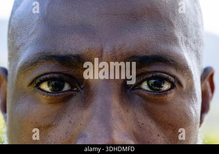 Uomo afroamericano maturo che mostra una texture facciale stretta e riflessi corneali dell'occhio all'aperto Foto Stock