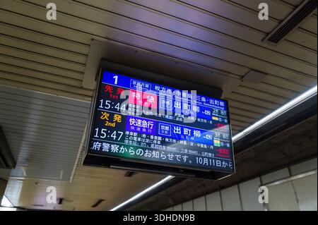 Osaka, Giappone - 15 ottobre 2023: Una scheda di partenza elettronica visualizza gli orari e le destinazioni dei treni in giapponese e inglese presso una stazione della metropolitana, mostrando orari, piattaforme e tipi di servizio sotto un soffitto con illuminazione fluorescente. Foto Stock