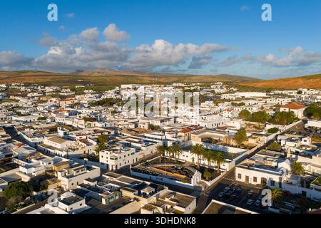 Vista aerea di edifici imbiancati raggruppati ermeticamente sotto un vasto cielo, in contrasto con il paesaggio arido che si estende oltre, Teguise, Isole Canarie, Foto Stock