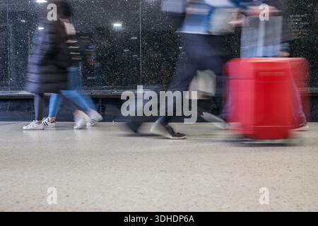 Viaggiatori offuscati che camminano con le valigie nel centro di transito. Londra, Regno Unito, 6 aprile 2024 Foto Stock
