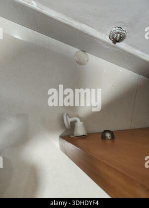Primo piano delle finiture del bagno sotto un soffitto inclinato, con doccia bianca e pomello metallico su ripiano in legno Foto Stock