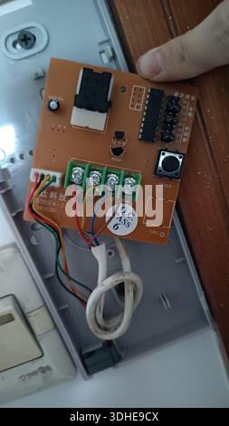 Tenere una mano su una scheda a circuiti stampati con cablaggio e componenti all'interno di una scatola elettrica Foto Stock