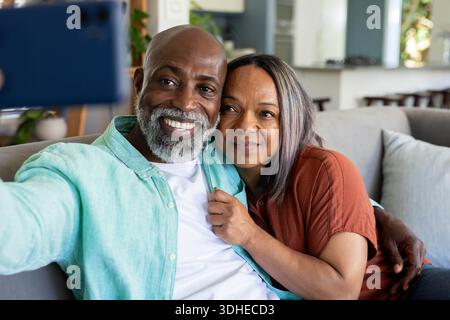 Diverse coppie senior che posano su un divano grigio chiaro con telefono blu, indossano camicetta ruggine e camicia color tè Foto Stock