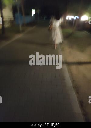Immagine notturna sfocata di una donna che cammina su un marciapiede Foto Stock