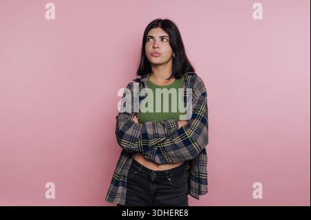 Giovane donna con braccia incrociate ed espressione scettica su sfondo rosa. Foto Stock