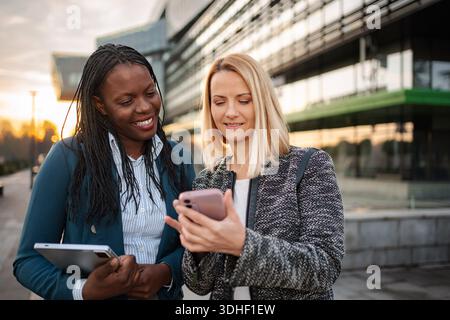 Donne d'affari diverse che discutono contenuti su smartphone e tablet all'aperto Foto Stock