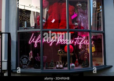 Un'affascinante vetrina a Saffron Walden, Essex, Regno Unito, con decorazioni natalizie e un vivace cartello al neon "la vita è bella" Foto Stock