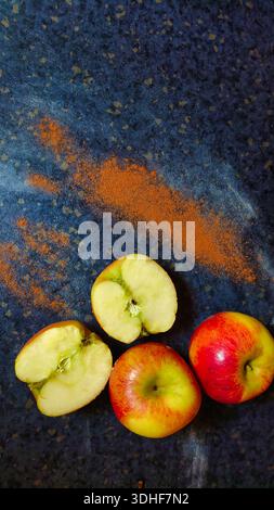 Un soffice strato piatto ad alto contrasto di mele fresche e spezie aromatiche su una superficie rustica scura. Perfetto per ricette di stagione, marchio di sidro e slow-l Foto Stock