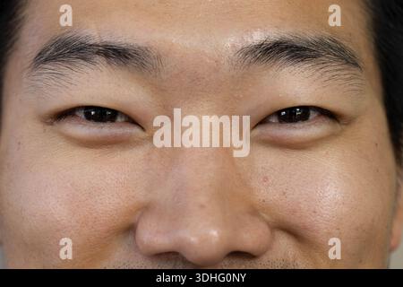 Uomo asiatico con gli occhi stretti in primo piano in studio, che mostra pori e barba leggera Foto Stock