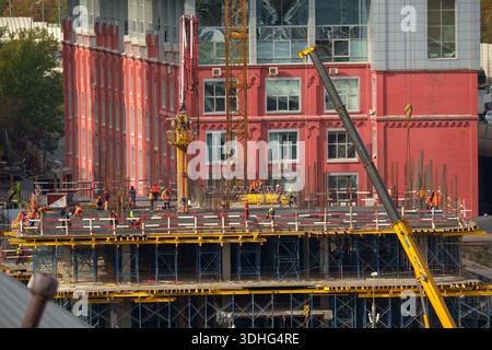 Gruppo di operai edili che operano in un cantiere urbano attivo con ponteggi, gru e strutture in calcestruzzo. Catturati con risoluzione elevata 7K Foto Stock