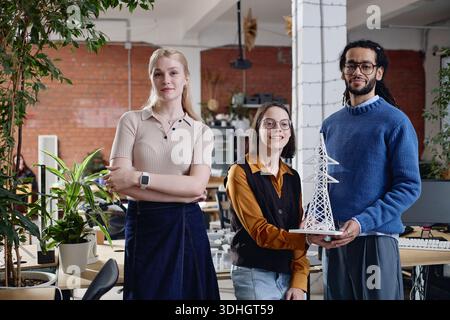 Tre giovani adulti colleghi multietnici che presentano il modello della torre di trasmissione Foto Stock