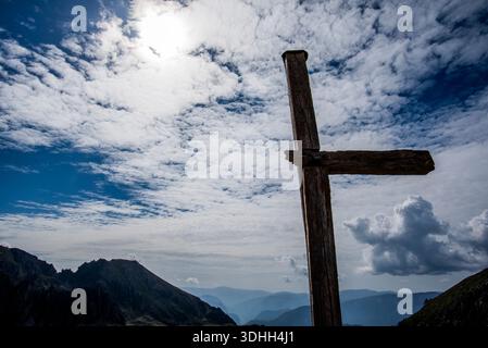 Antica croce di legno sagomata contro un cielo luminoso con nuvole spettacolari sui monti del Lagorai in Trentino, creando un'impressionante alta altitude Foto Stock