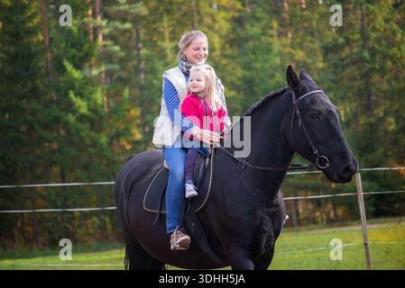 Madre e figlia gioiose che si godono un rilassante giro a cavallo in aperta campagna, circondati dai colori autunnali. Immagine orizzontale che rappresenta la funzione fa semplice Foto Stock