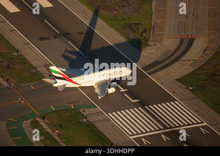 San Francisco, Stati Uniti - 22 novembre 2025: Veduta aerea di un aereo Emirates che proietta una lunga ombra mentre decolla dalla pista, luce del sole Foto Stock