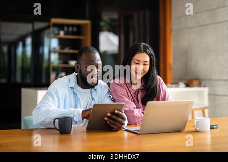 Team aziendale, due manager eterogenei e felici che lavorano insieme utilizzando un notebook in ufficio. Foto Stock