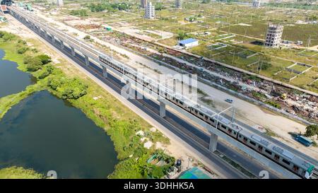 Veduta aerea di un moderno treno della metropolitana che scivola lungo i binari sopraelevati vicino a dia Bari Road, in contrasto con il verde circostante, Dacca, Divisione di Dacca Foto Stock