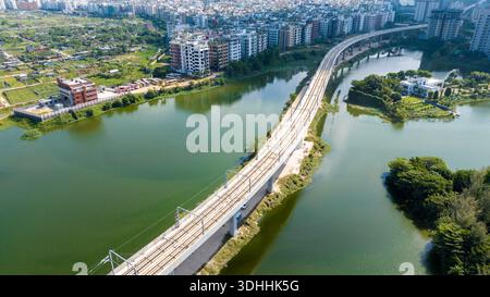 Vista aerea di un binario ferroviario che attraversa un lago tranquillo, che riflette il cielo e gli edifici circostanti, dia Bari Road, Dhaka, Dhaka Division, Bangla Foto Stock