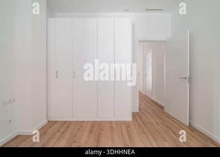 Un interno luminoso e minimalista caratterizzato da un armadio bianco e pavimento in legno. Le pareti sono semplici e lo spazio è ordinato, sottolineando la semplicità Foto Stock