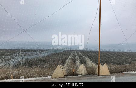 Una rete anti-drone è appesa sulle linee difensive nella regione di Charkiv. File di denti di drago in cemento e bobine di filo metallico si estendono sul campo. Foto Stock