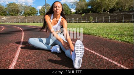 Giovane donna atletica che allunga le gambe su una pista da corsa prima di allenarsi Foto Stock