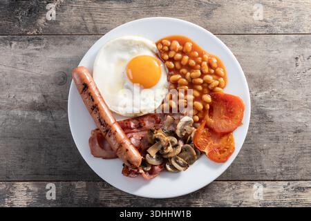 Colazione all'inglese completa con uova fritte, pancetta, salsicce e fagioli su un tavolo di legno. Foto Stock