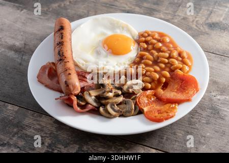 Colazione all'inglese completa con uova fritte, pancetta, salsicce e fagioli su un tavolo di legno. Foto Stock