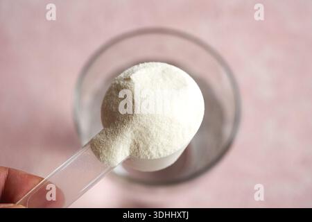 Mano che tiene una paletta di polvere di collagene sopra un bicchiere d'acqua. Integratore nutrizionale. Foto Stock