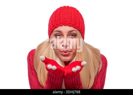 Una donna vestita con caldi abiti invernali rossi che soffiano un bacio su uno sfondo bianco. Foto Stock