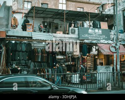 Negozio di abbigliamento tradizionale nel centro di Amman, Giordania. Vista sulla strada di un negozio con abiti esposti e un uomo che riposa su un balcone sopra. Medio Oriente. Foto Stock