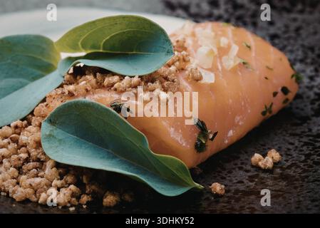 Un filetto di salmone ben placcato guarnito con erbe fresche e un condimento con briciole, servito su un piatto scuro. Foto Stock