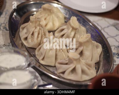 Gnocchi khinkali tradizionali georgiani serviti su un piatto di metallo con pepe nero, panna acida e stoviglie rustiche, cucina adatta per il ristorante Foto Stock