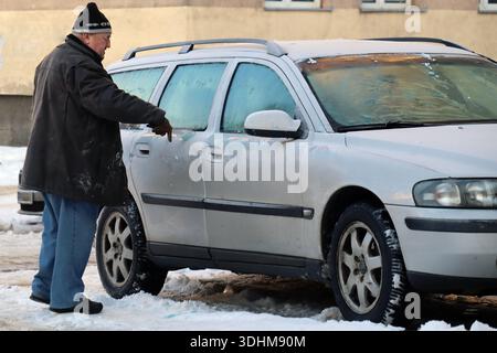 Un uomo che pulisce la neve dalla sua auto ghiacciata in una fredda giornata invernale. Foto Stock