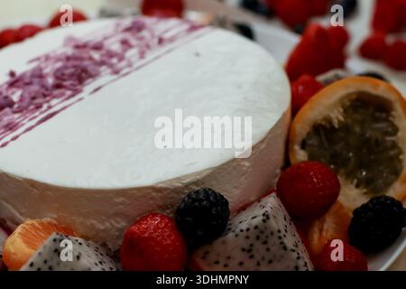 Dettagli mirati sul dessert bianco rotondo condito in viola, guarnito con frutti di bosco, fette di frutta drago e metà di agrumi su un piatto Foto Stock